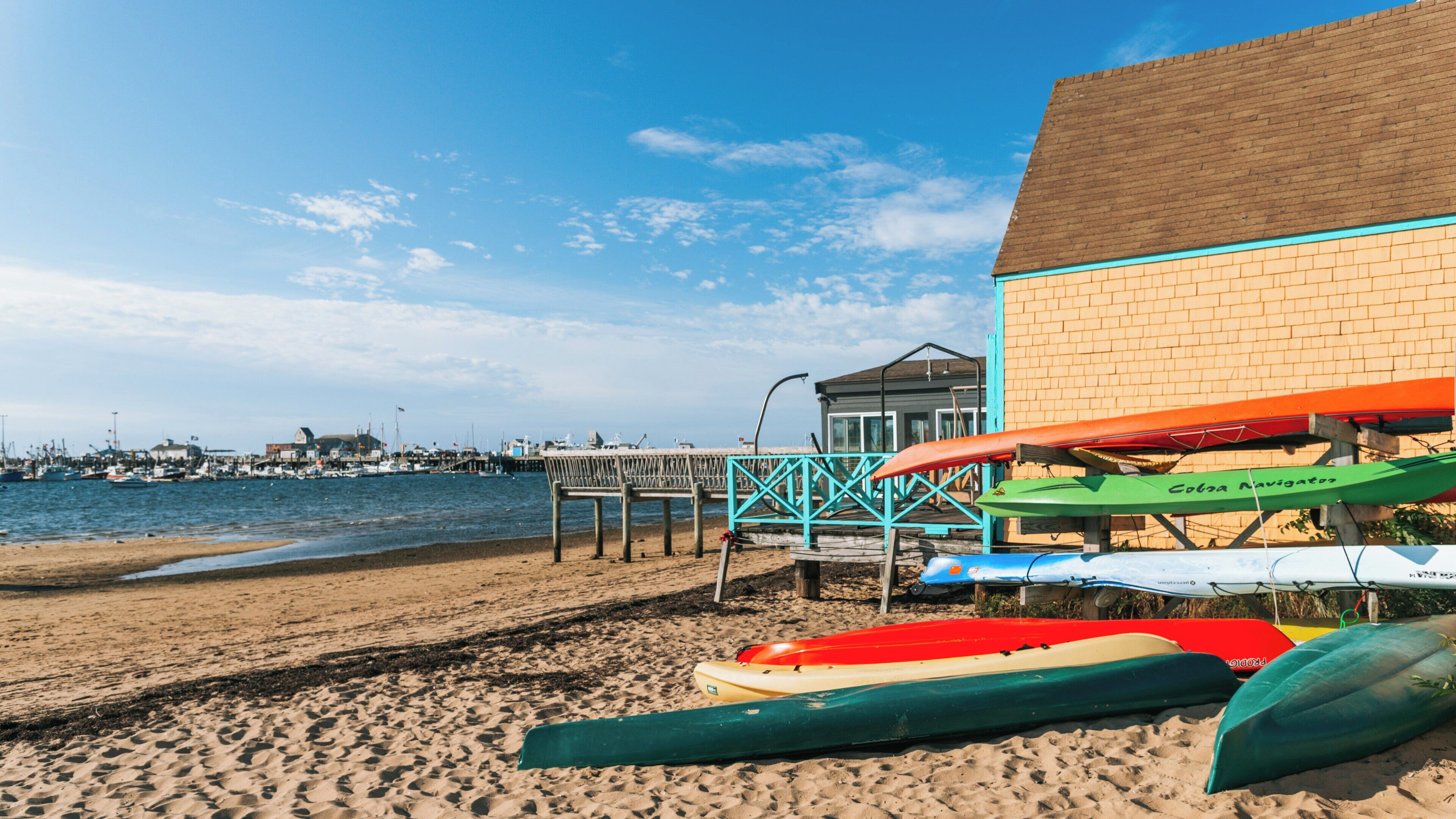 Colorful kayaks rest on the sandy beach near MacMillan Pier in Provincetown, Massachusetts on a clear day with bright blue skies