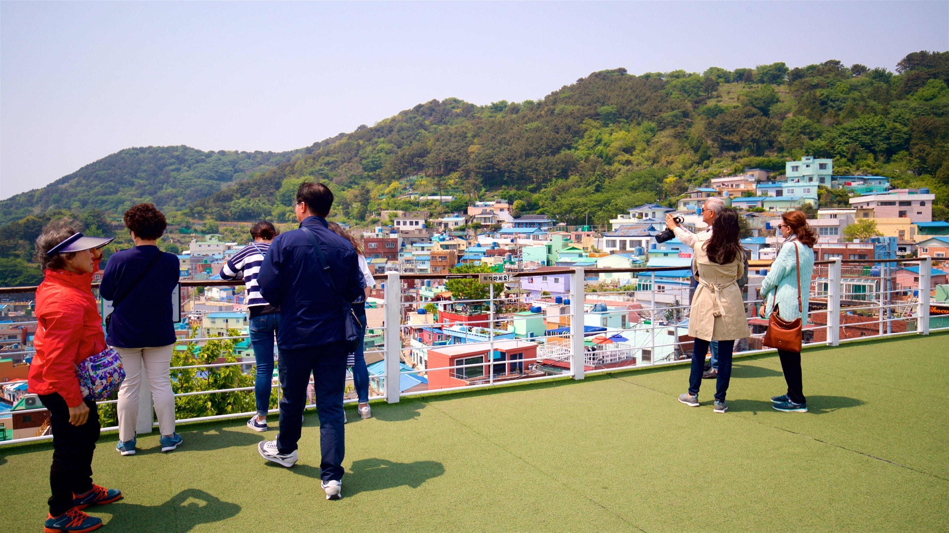 A group of people on a viewing platform overlooking a hillside with colorful buildings.