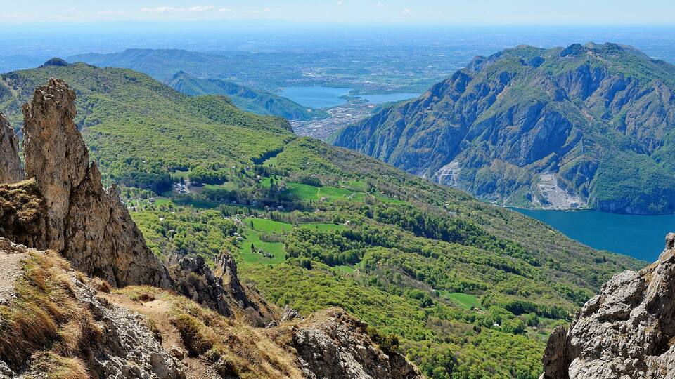 A mountainous landscape with a valley, a lake, and a prominent rock formation.
