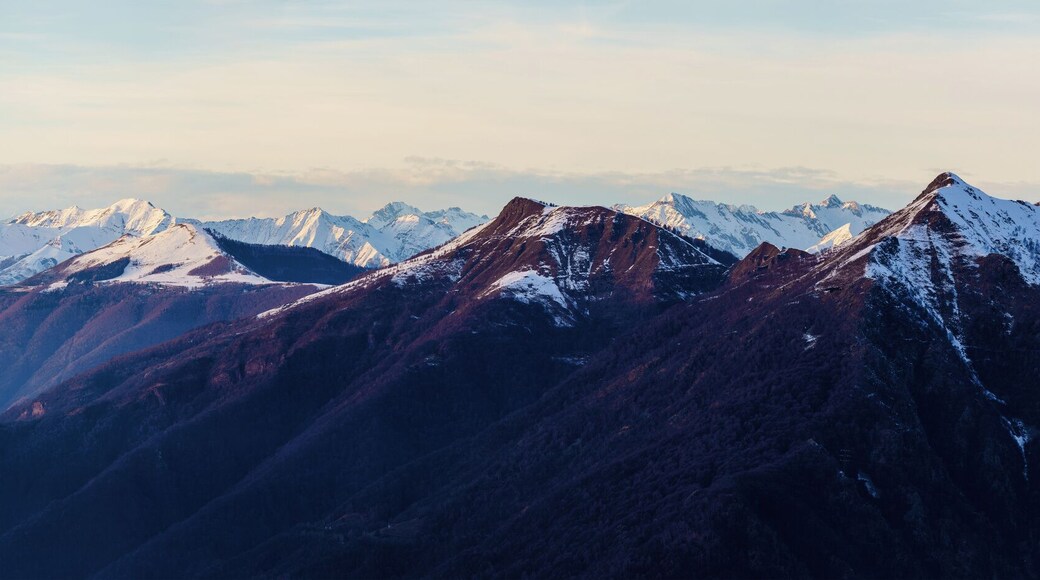Misty valley lies beneath snow-capped mountain peaks at dusk near Piani di Bobbio in Italy, with soft light creating serene and tranquil alpine landscape