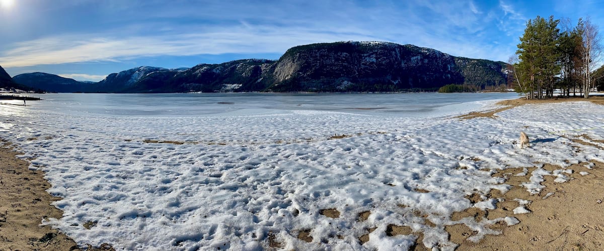 A frozen lake with snow-covered ground, mountains in the background, and a clear sky.