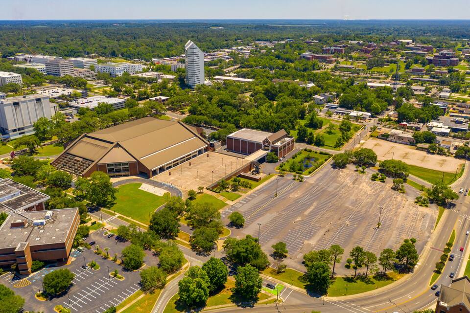 An aerial view of a campus with buildings, parking lots, and surrounding greenery.