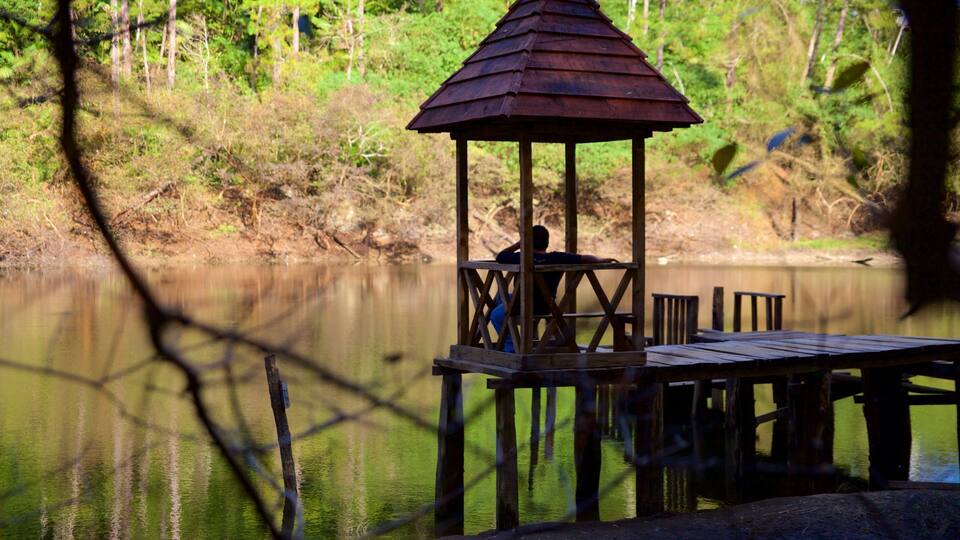 A wooden gazebo by a calm lake surrounded by trees.