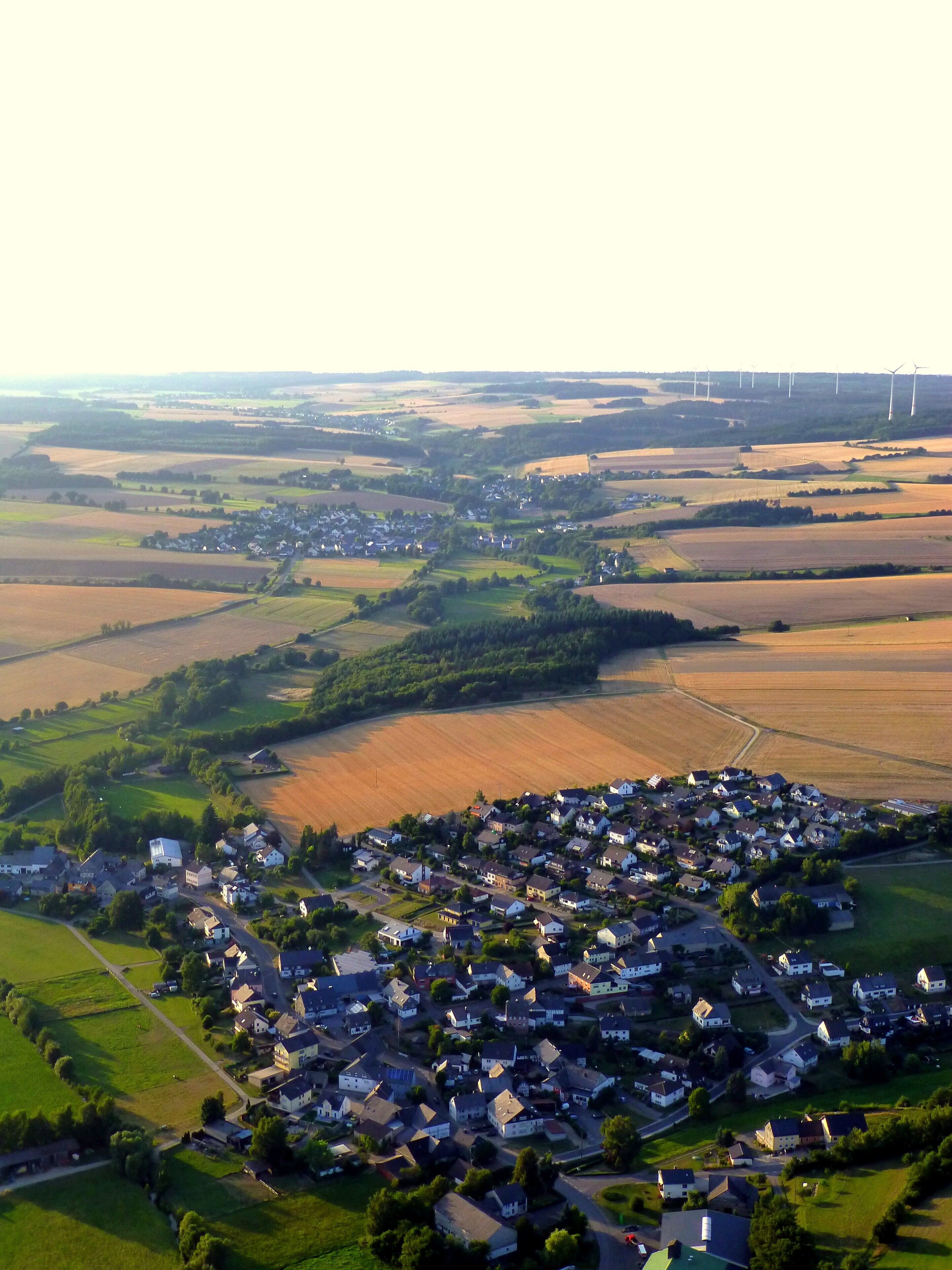 Vista aérea de un pueblo rural con aerogeneradores a lo lejos.