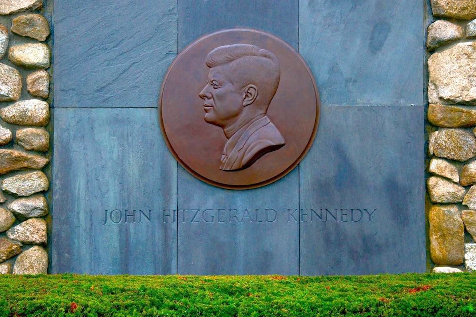 A memorial plaque with a bust of John F. Kennedy surrounded by a stone wall.