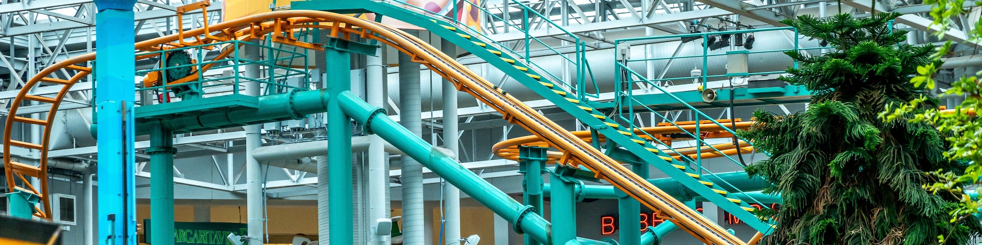 A roller coaster with a large mascot figure, a green tree, and industrial structures.