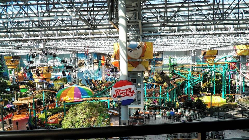 An indoor amusement park with roller coasters, a Pepsi Cola sign, and various rides.