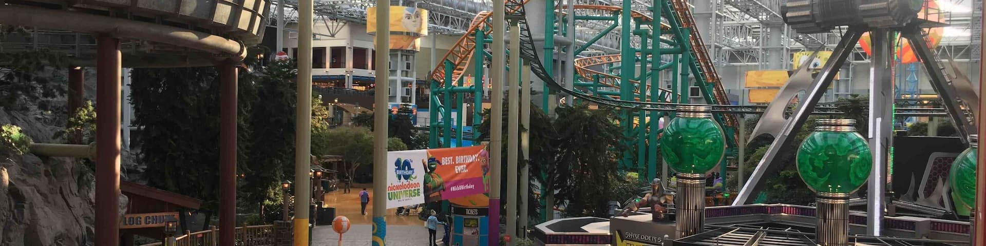 An indoor amusement park with roller coasters, a green ball ride, and various shops.