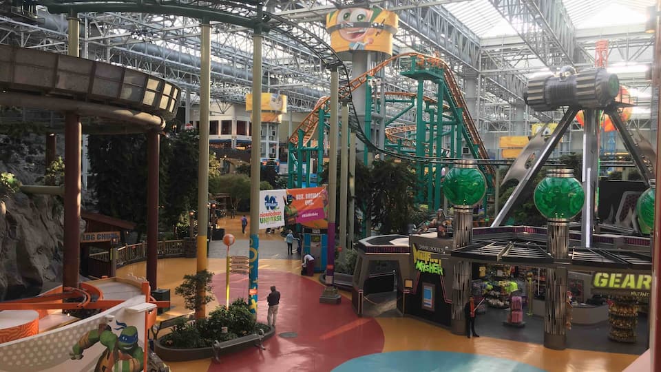 An indoor amusement park with roller coasters, a green ball ride, and various shops.