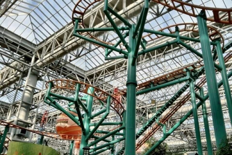 Un gran parque de atracciones cubierto con techo de cristal y vías de montañas rusas.