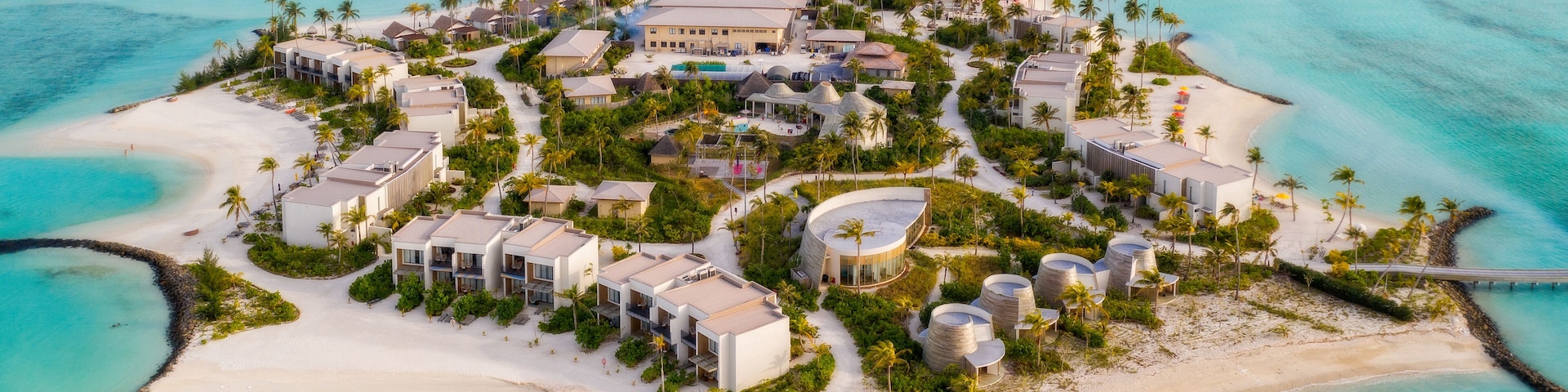 Vista aérea de un complejo turístico con bungalows sobre el agua, una playa y aguas turquesas cristalinas.