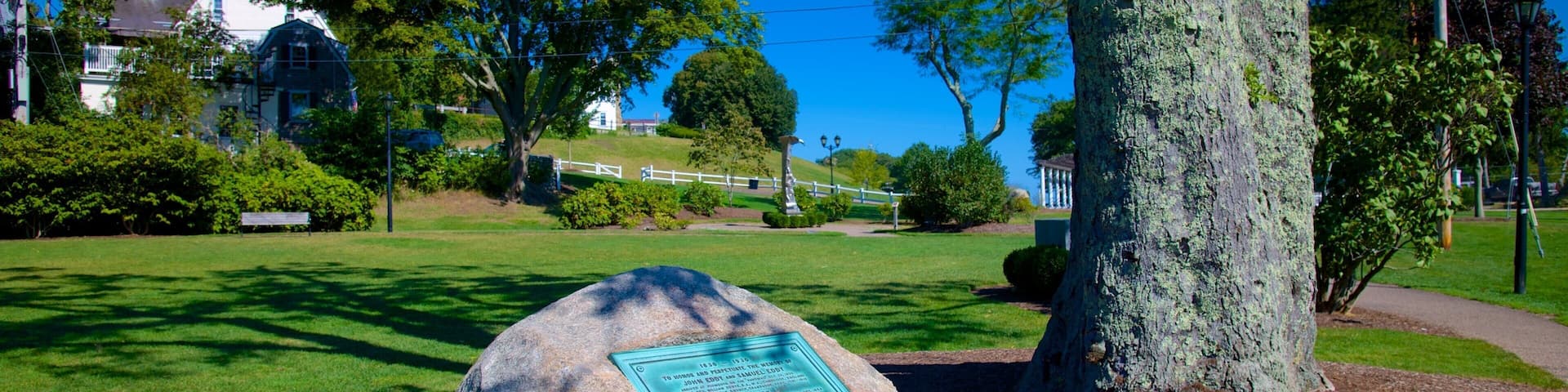 A park with a large stone monument, trees, a white fence, and a clear blue sky.