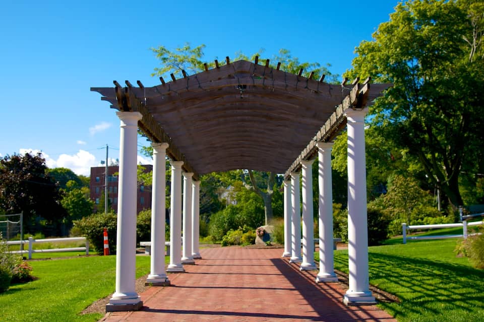A covered walkway with white columns, surrounded by greenery and trees.