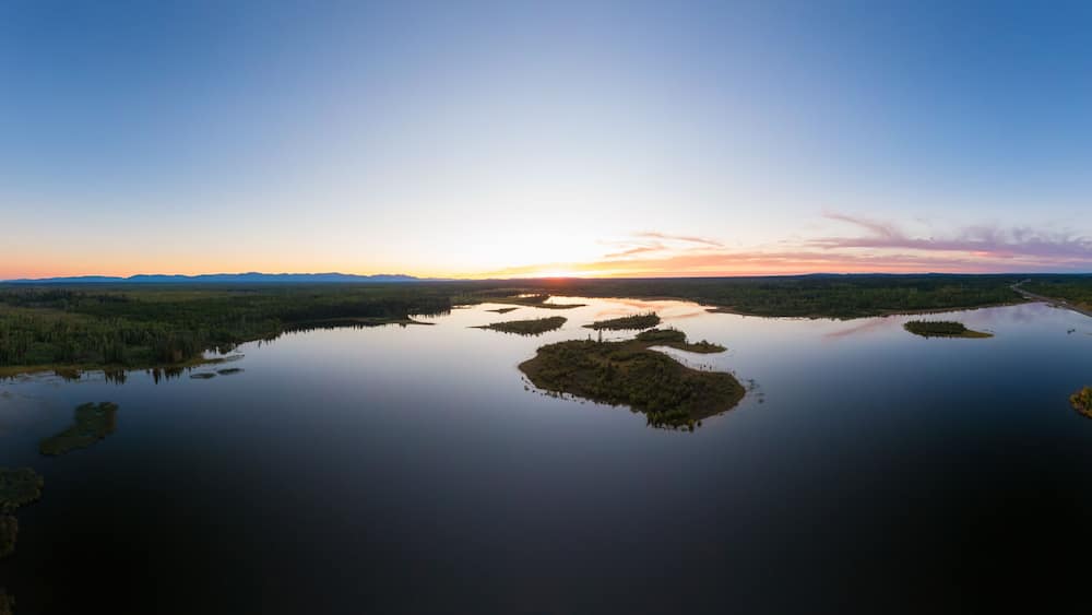 A calm lake with several small islands surrounded by dense forests, under a clear sky.