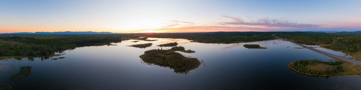 A calm lake with several small islands surrounded by dense forests, under a clear sky.