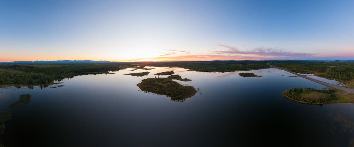 Tyyni järvi, jossa on useita pieniä saaria, ja järveä ympäröivät tiheät metsät. Taivas on kirkas.