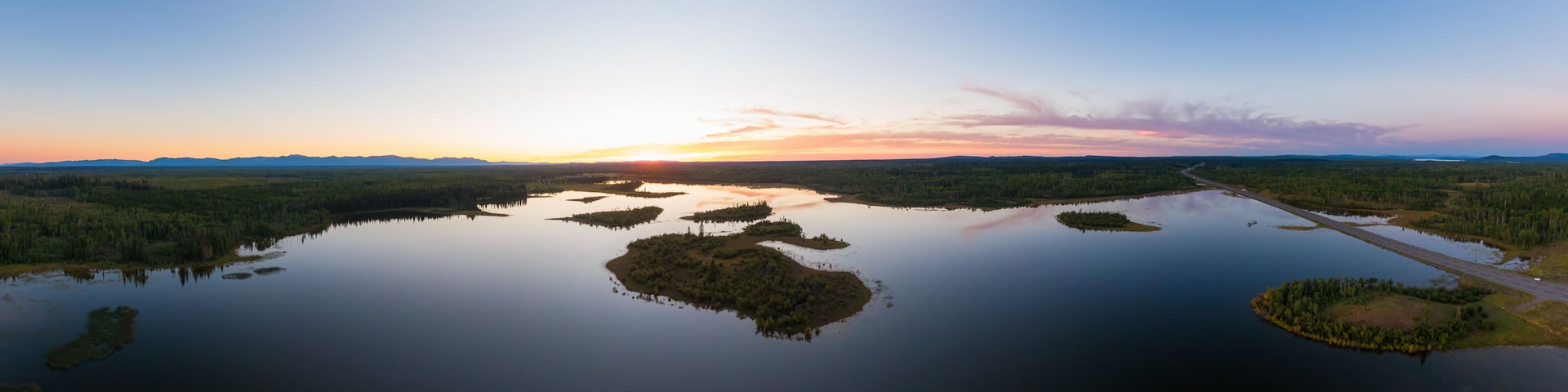 Um lago calmo com várias ilhotas, cercado por florestas densas, sob um céu claro.