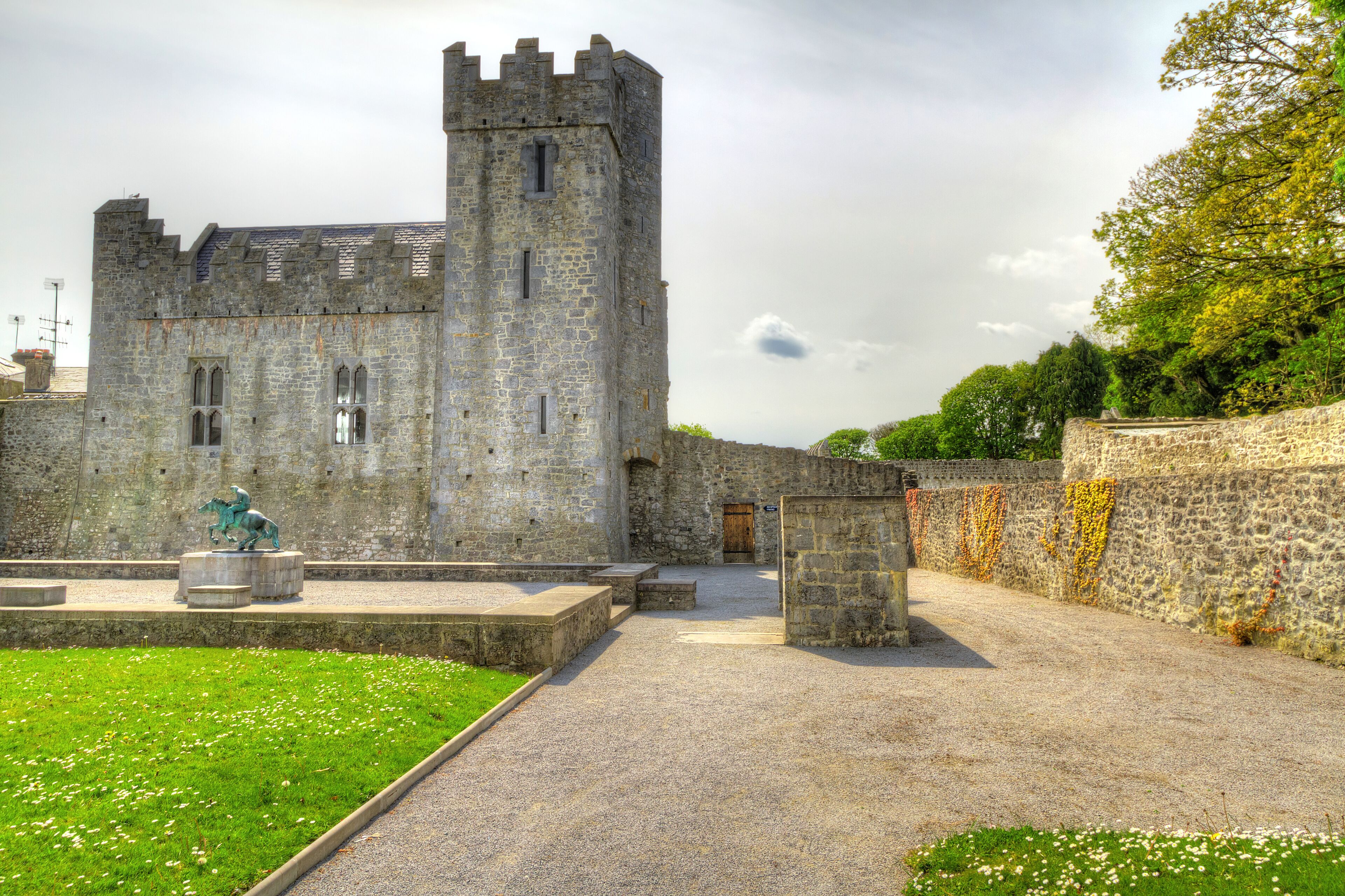 A historic stone castle with a tower, a statue, and a paved pathway.