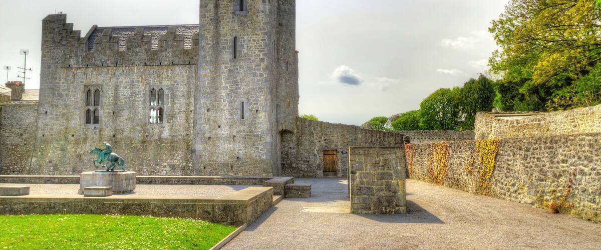 A historic stone castle with a tower, a statue, and a paved pathway.