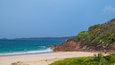 A beach with clear turquoise water, sandy shore, and a rocky cliff with greenery.