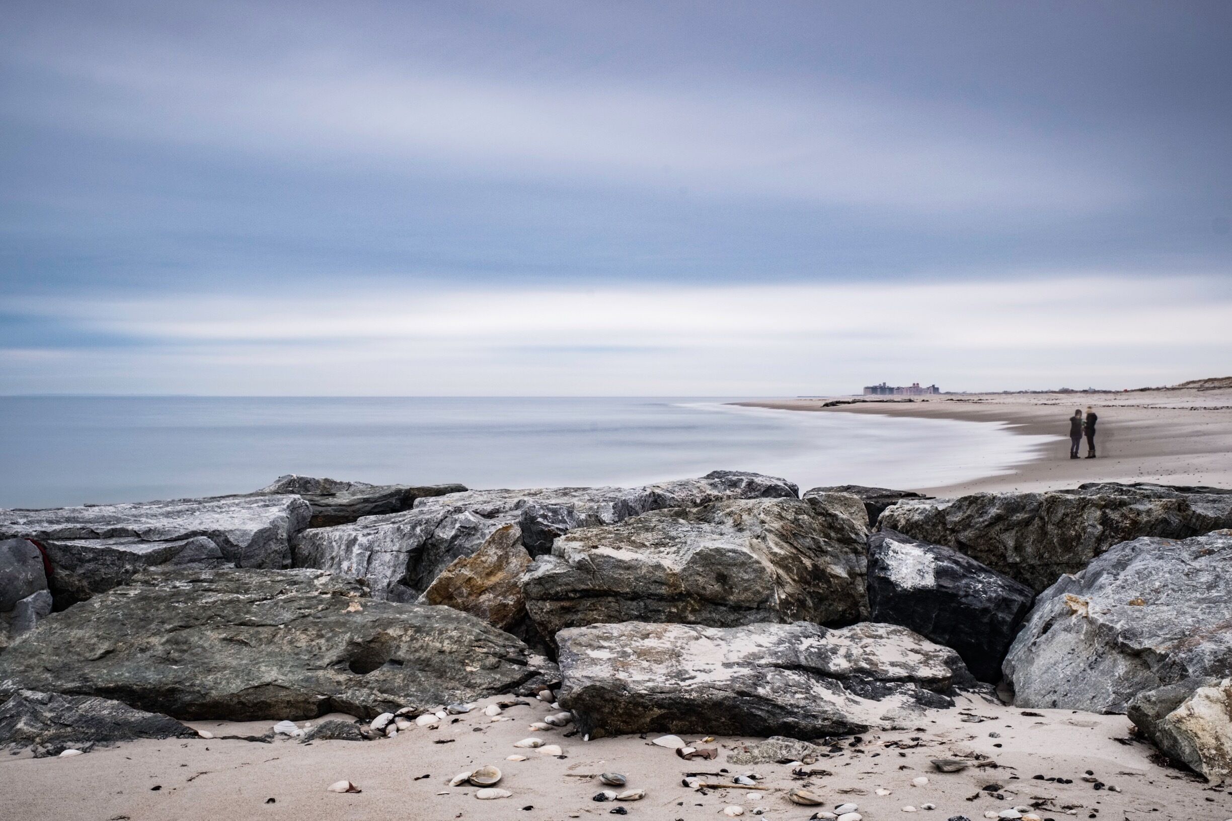A rocky beach with large boulders in the foreground and a calm sea in the background.