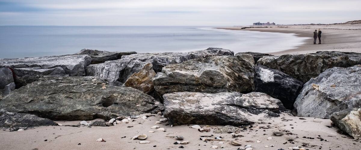 A rocky beach with large boulders in the foreground and a calm sea in the background.