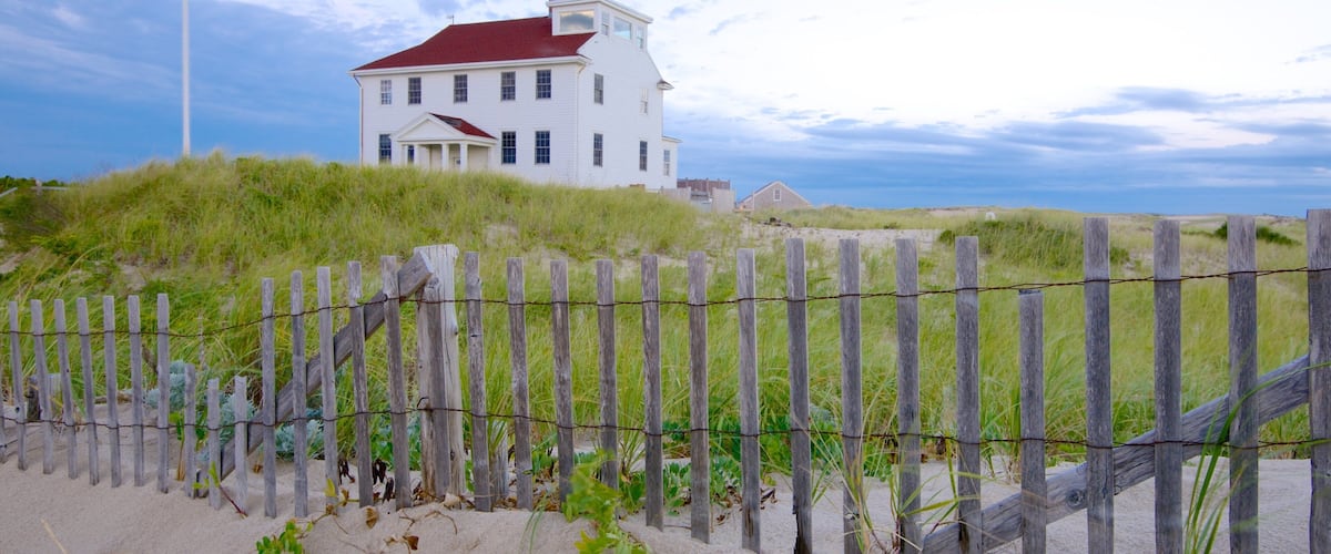 A white house with a red roof on a grassy hill.