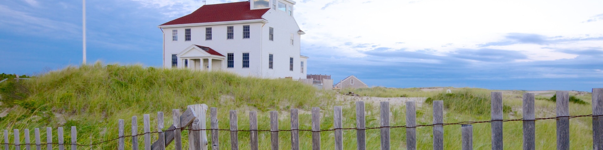 A white house with a red roof on a grassy hill.