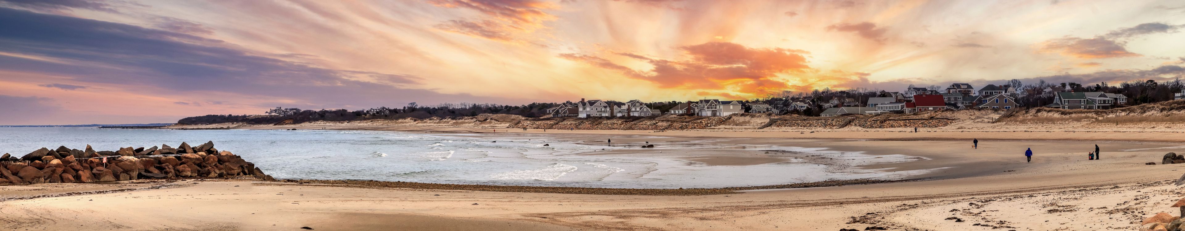 Una playa con un atardecer, olas y casas a lo largo de la costa.