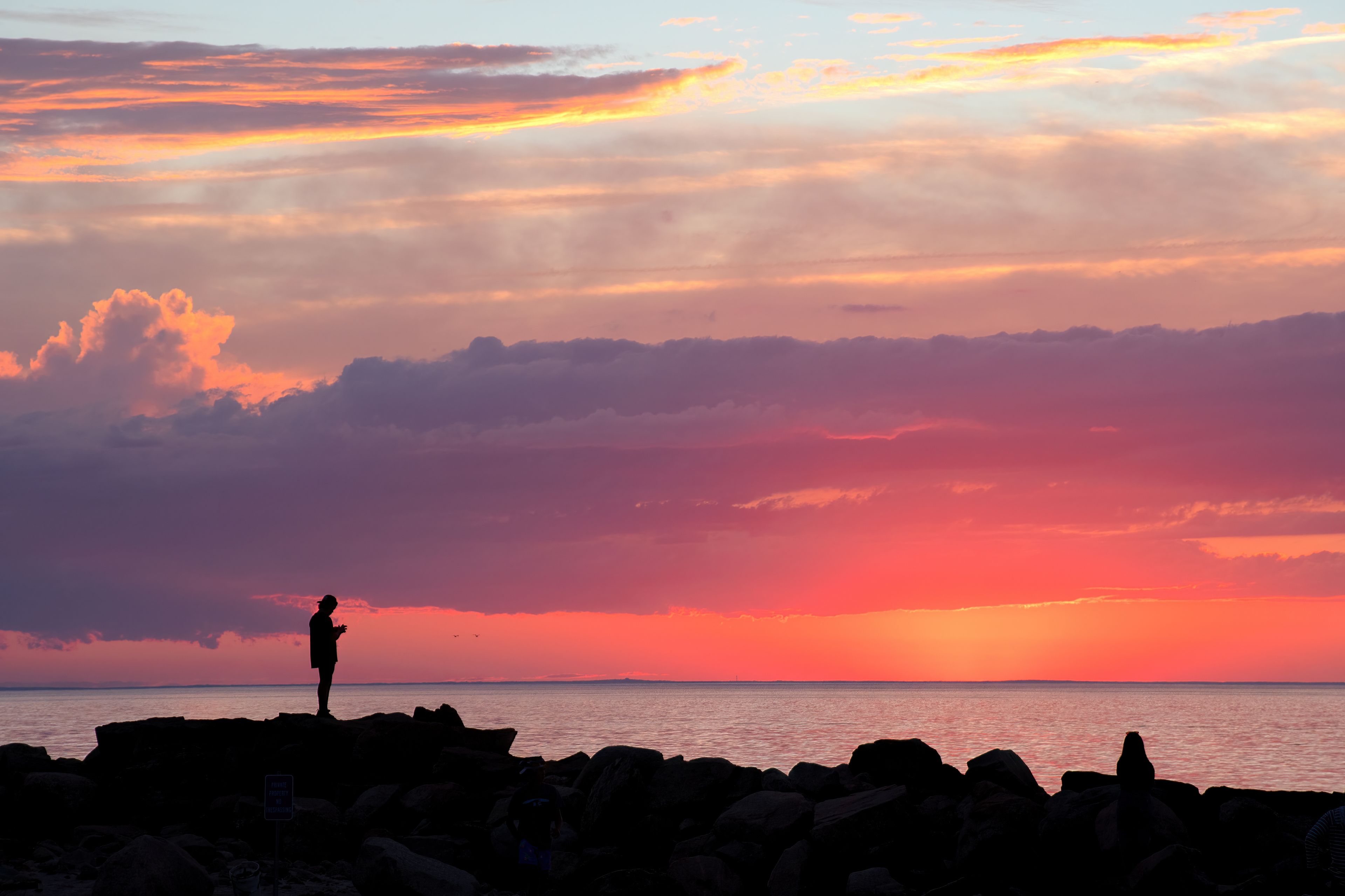 Silueta de una persona de pie sobre rocas al atardecer, con un cielo vibrante.