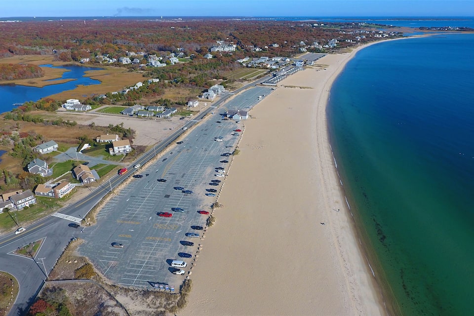 A coastal town with a long beach, parking lot, and a road leading to the beach.