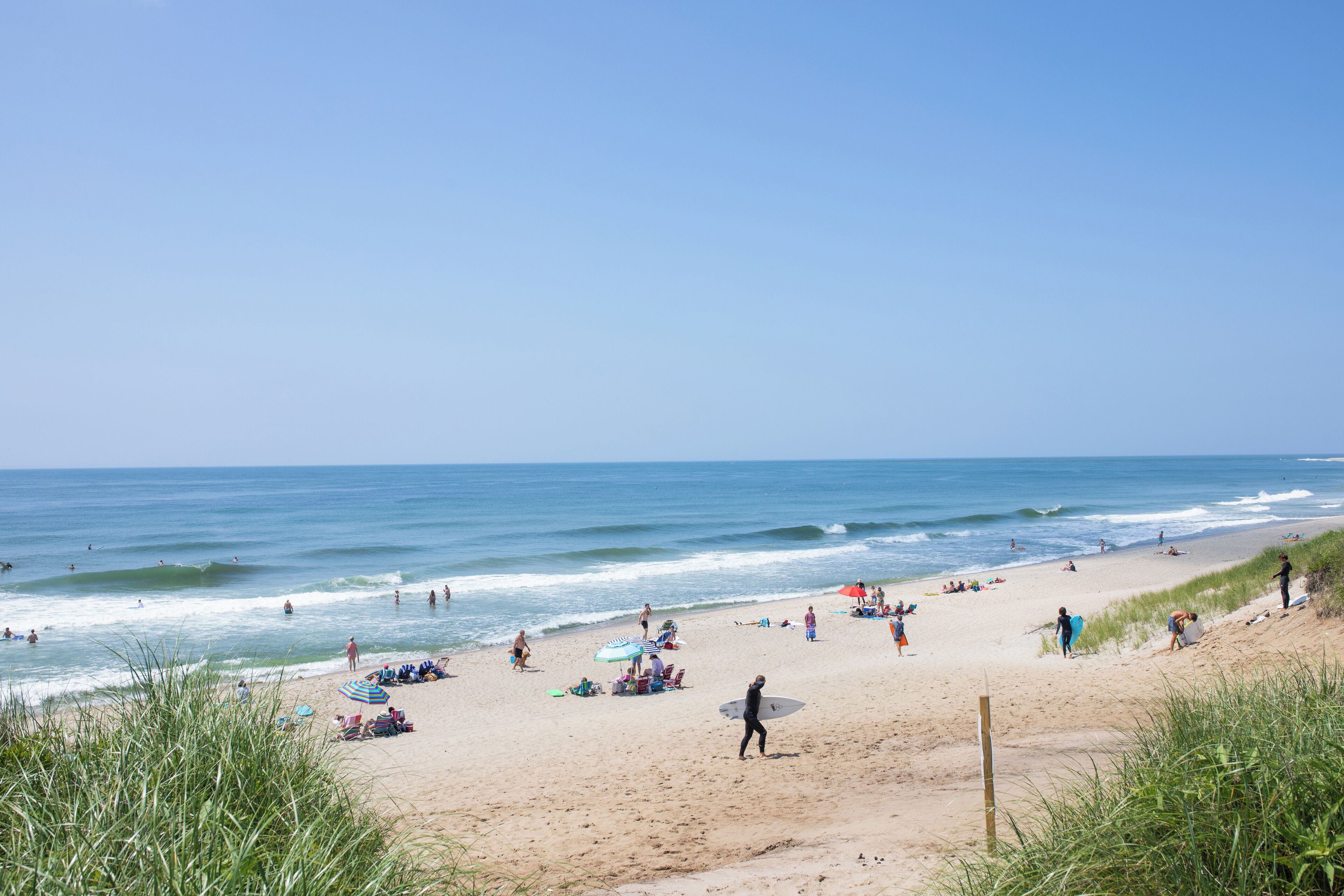 A beach with people, umbrellas, and surfboards.