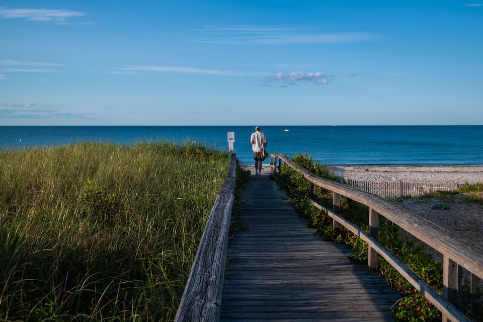 A wooden boardwalk leading to a beach with a person walking away from the camera.