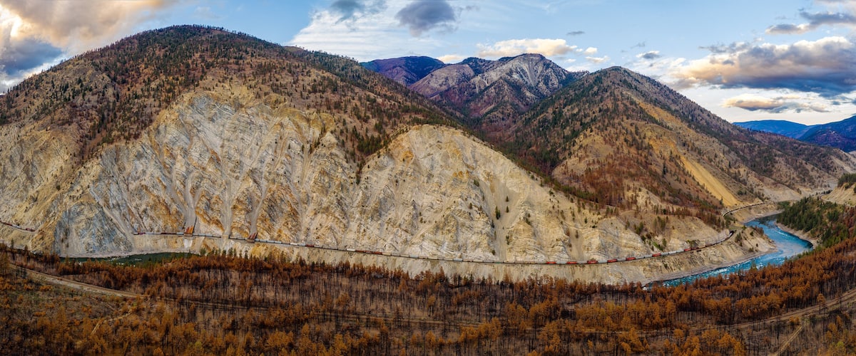 A mountainous landscape with a winding train track and a river.