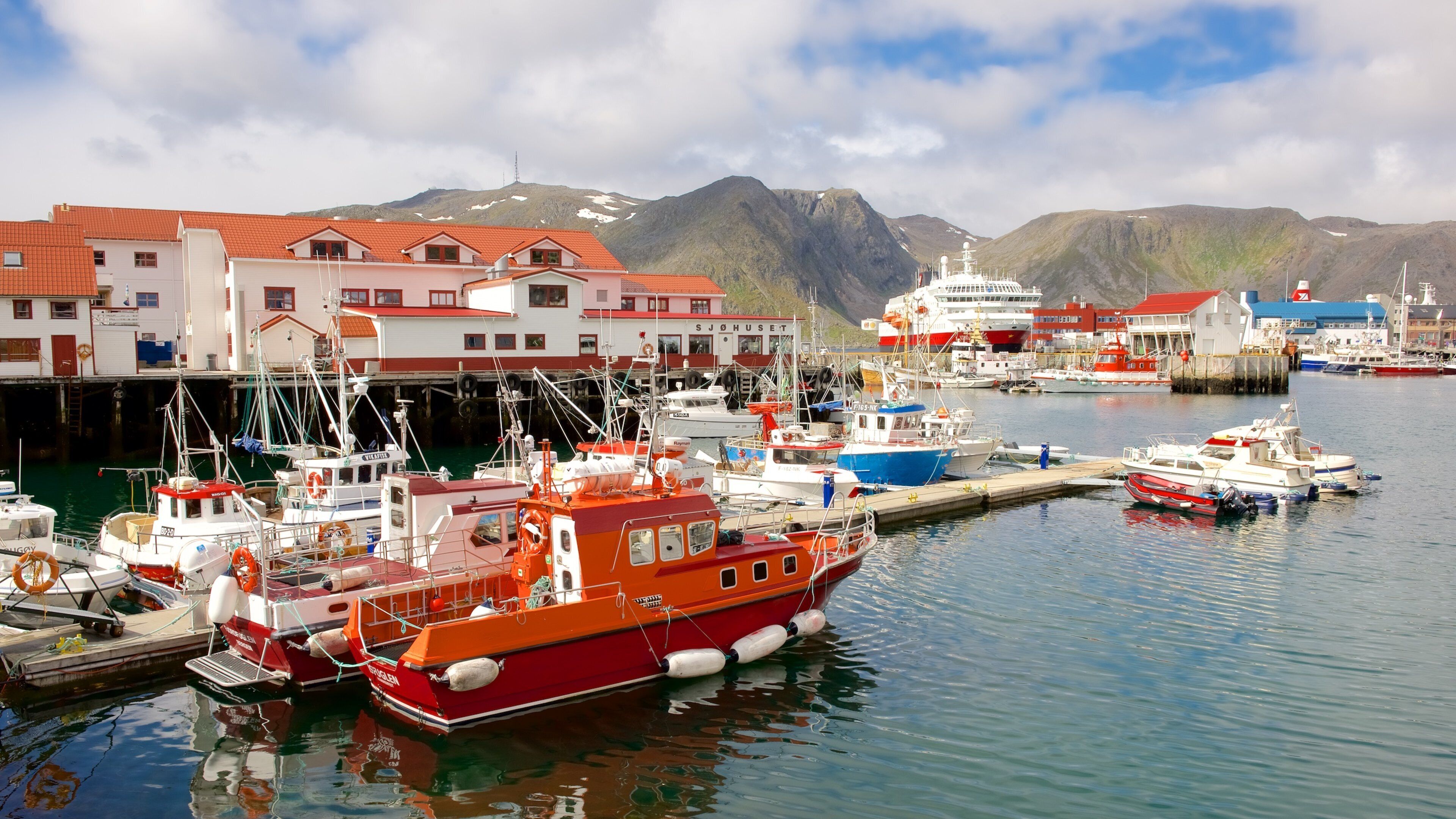 A harbor with boats, buildings, and mountains in the background.