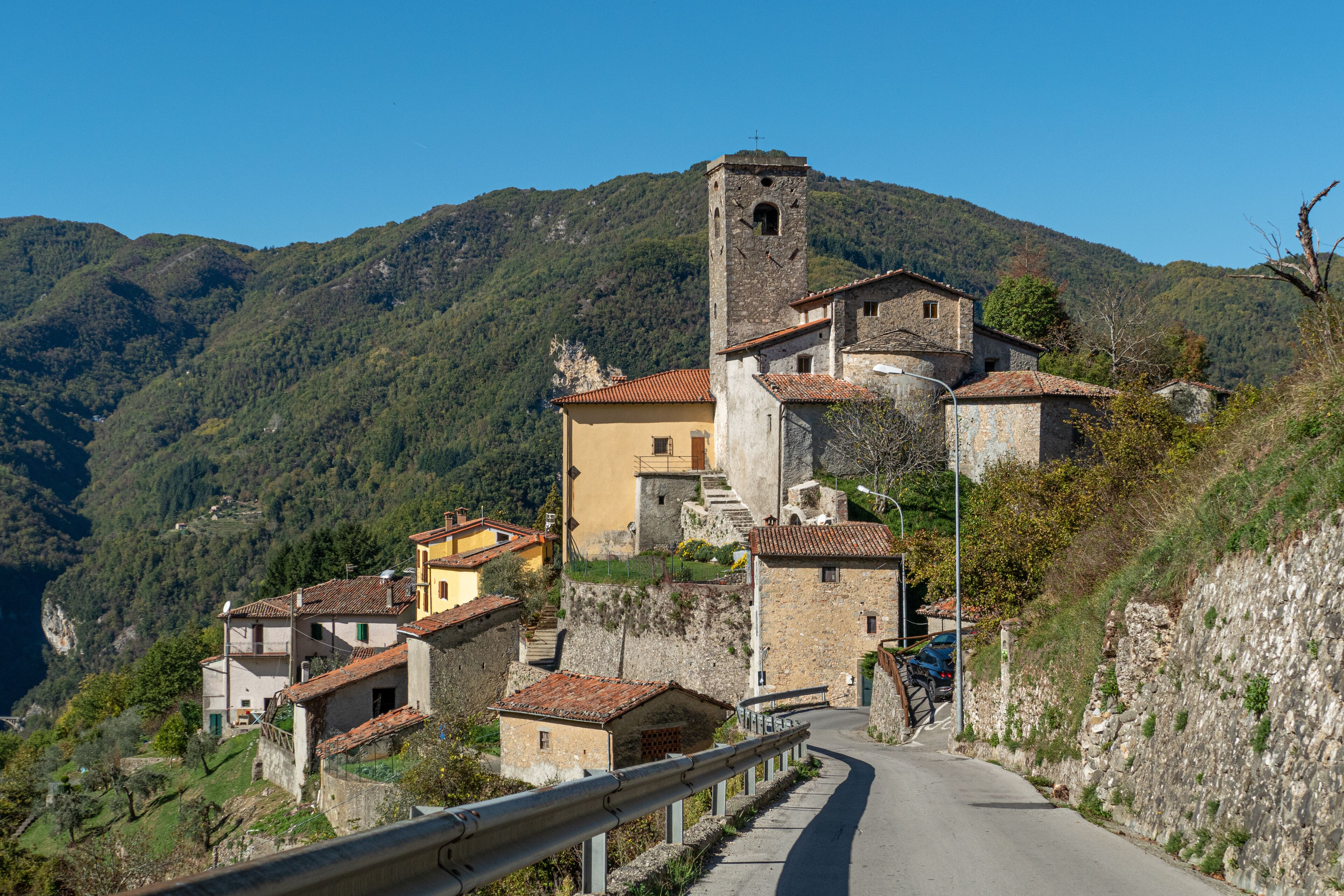 A winding road through a mountainous village with stone buildings and a church tower.