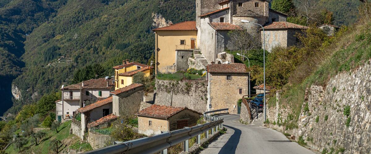 A winding road through a mountainous village with stone buildings and a church tower.
