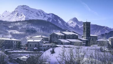 A snow-covered village with stone buildings and a church tower against a backdrop of snow-capped mountains.