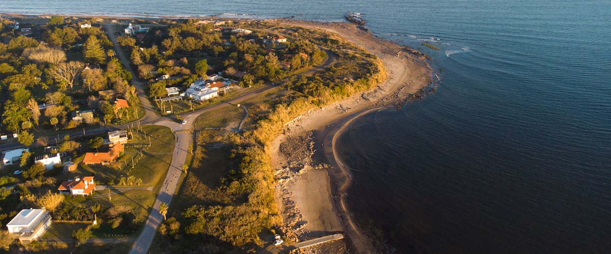 An aerial view of a coastal area with a curved shoreline, a road, and residential buildings.