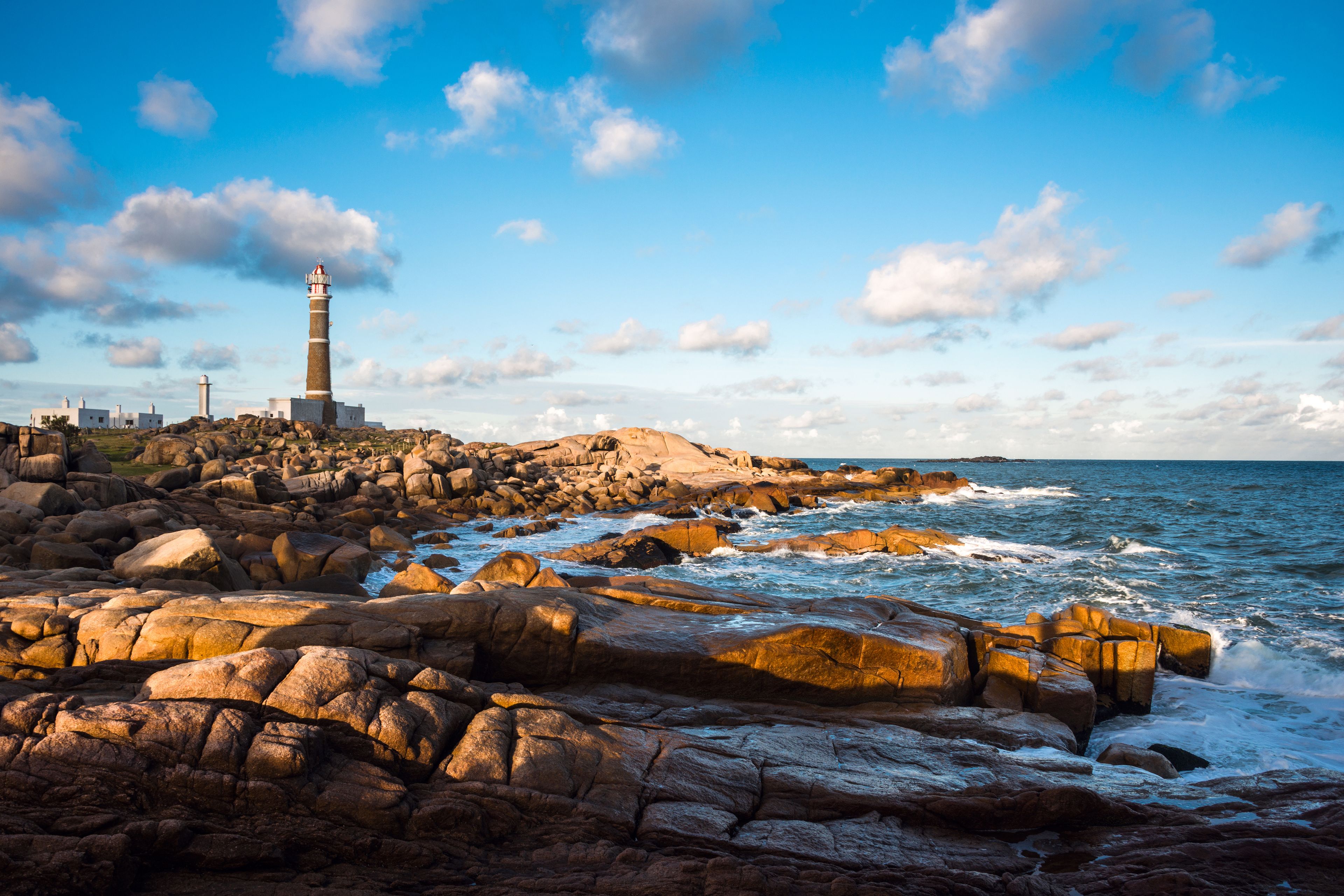 A rocky coastline with a lighthouse and waves crashing against the rocks.
