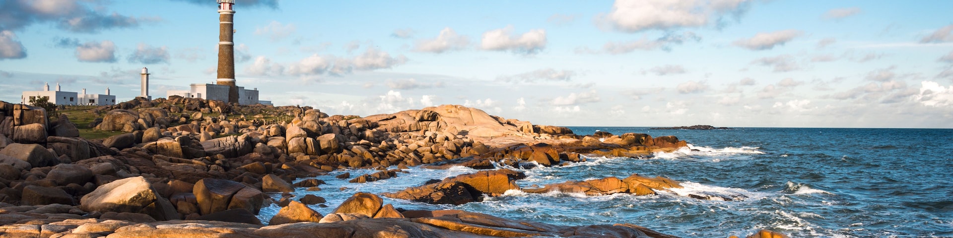 A rocky coastline with a lighthouse and waves crashing against the rocks.