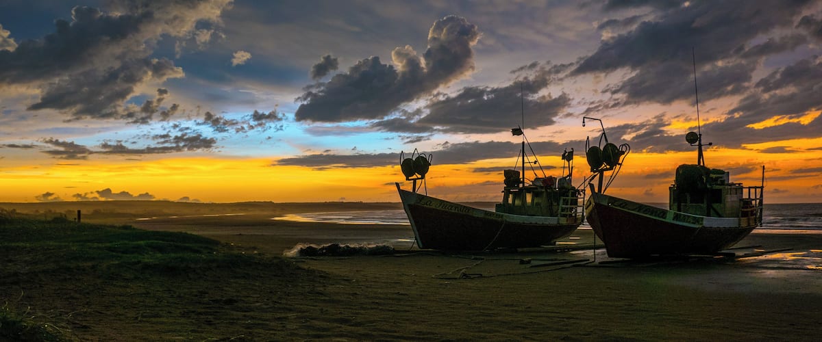 Two boats on a beach with a sunset in the background.