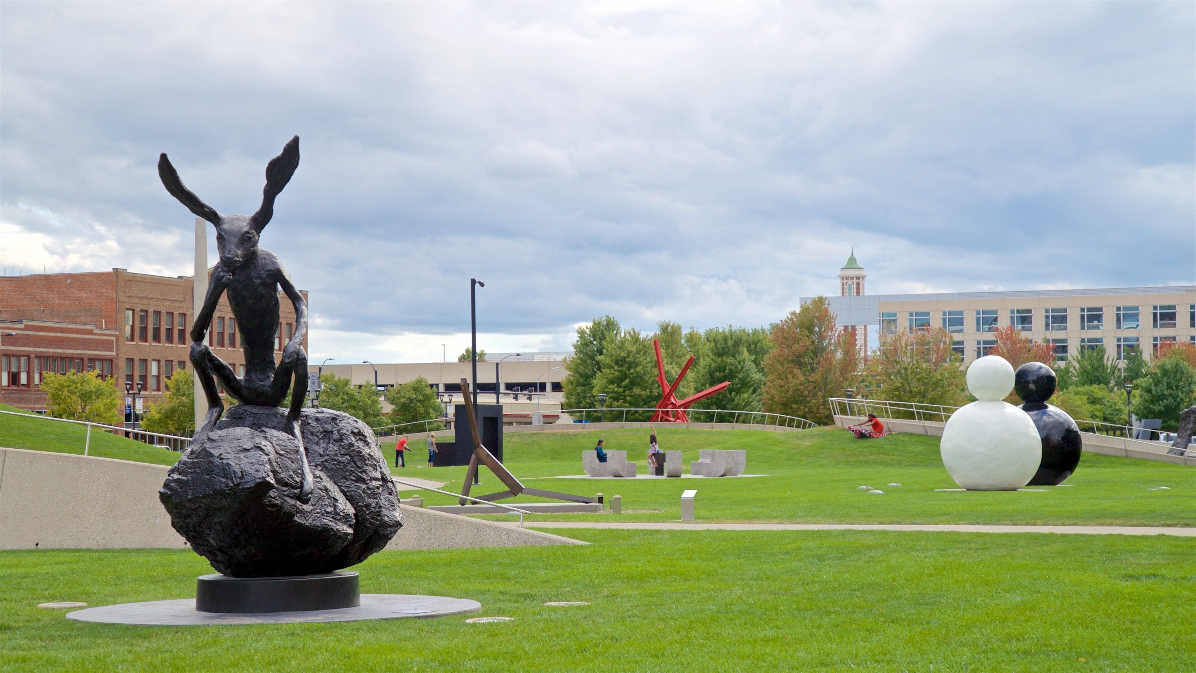 A sculpture of a horse on a rock, a large spherical sculpture, and a building with a clock tower in the background.