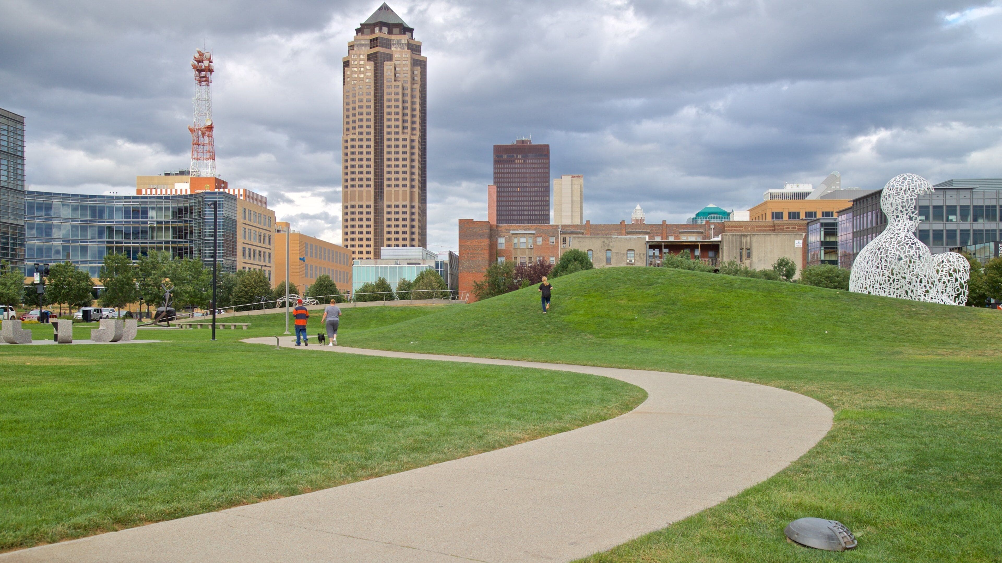 A park with a winding path, a grassy hill, and a city skyline in the background.