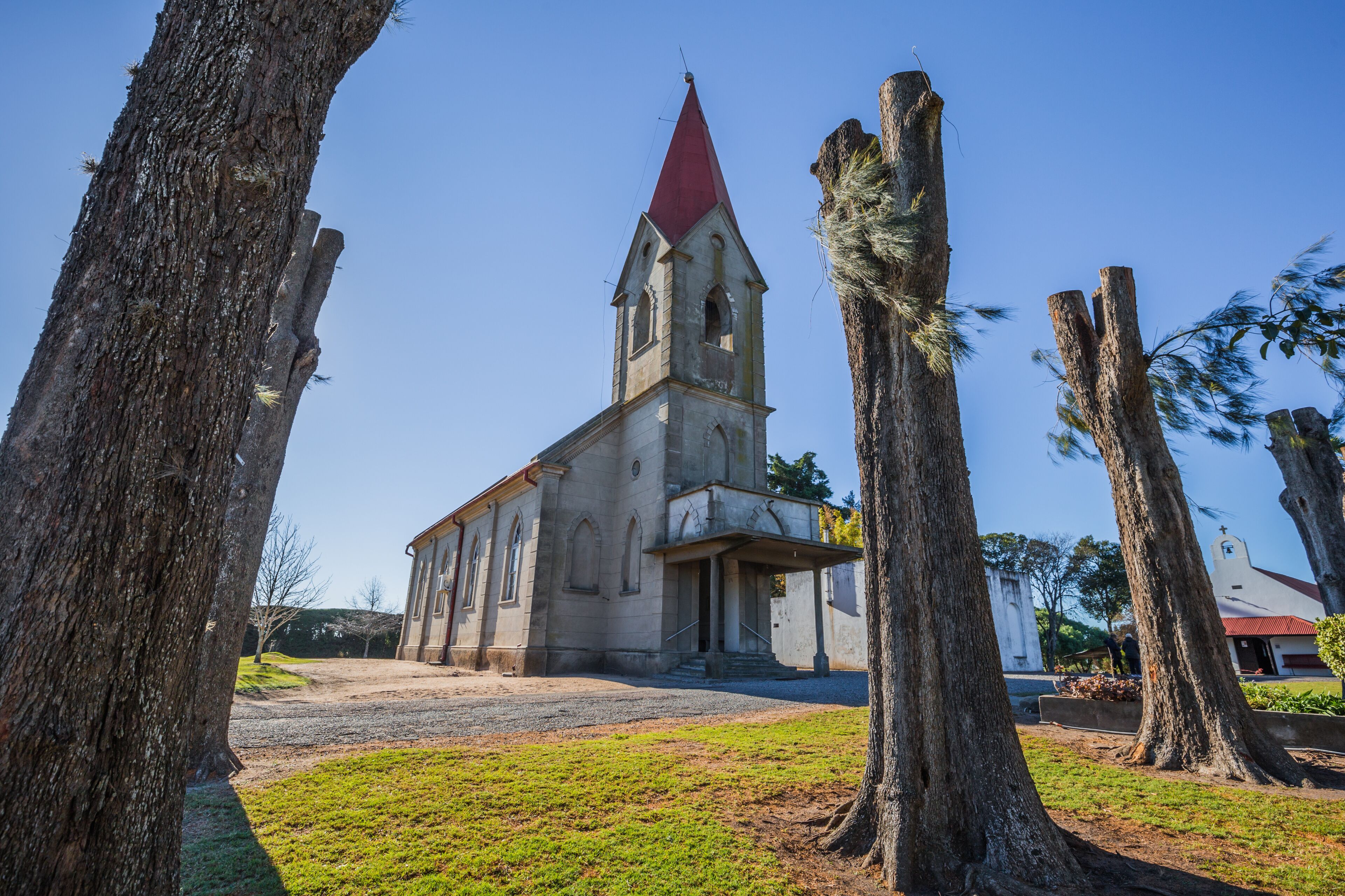 A church with a red roof and a bell tower, surrounded by trees and a clear sky.