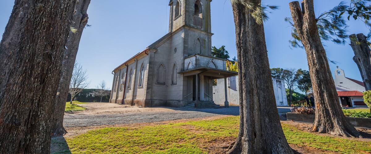 A church with a red roof and a bell tower, surrounded by trees and a clear sky.
