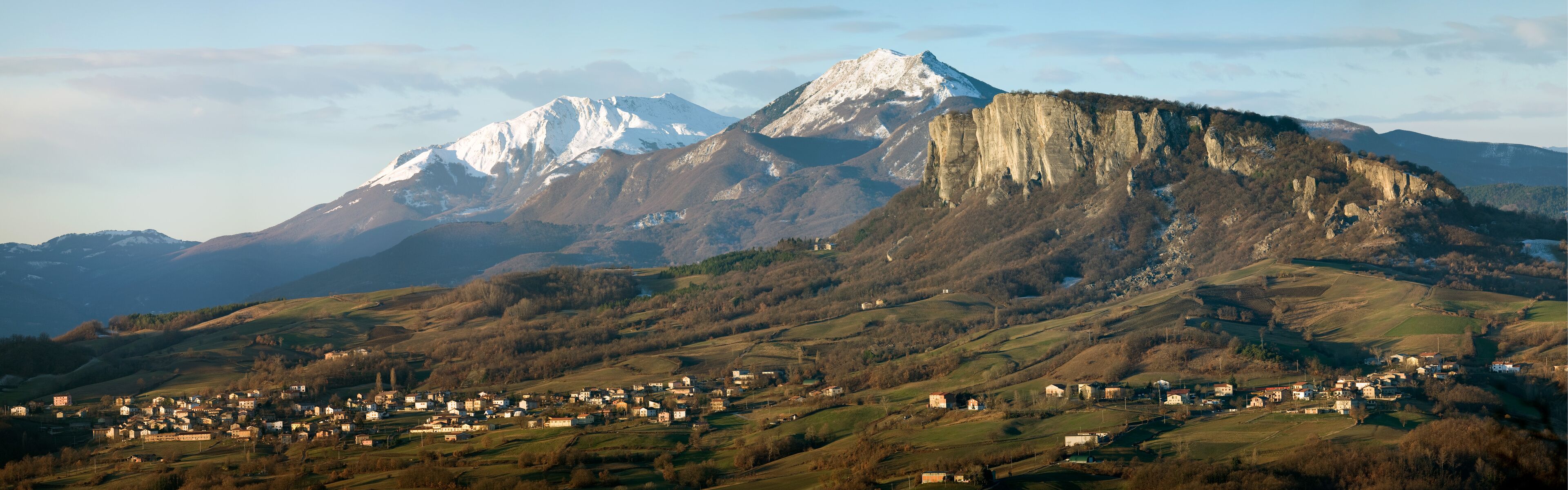 A mountainous landscape with a village in the foreground and snow-capped peaks in the background.