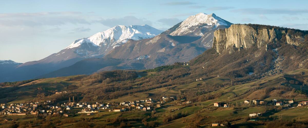 A mountainous landscape with a village in the foreground and snow-capped peaks in the background.