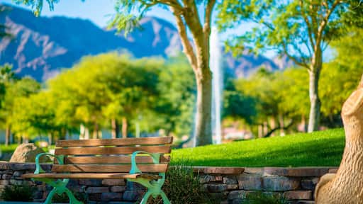 A park bench with a stone wall and grass, surrounded by trees and mountains in the background.