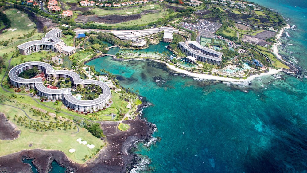 Luftaufnahme eines Küstenresorts mit mehreren Gebäuden, einem Golfplatz und klarem, blauem Wasser.